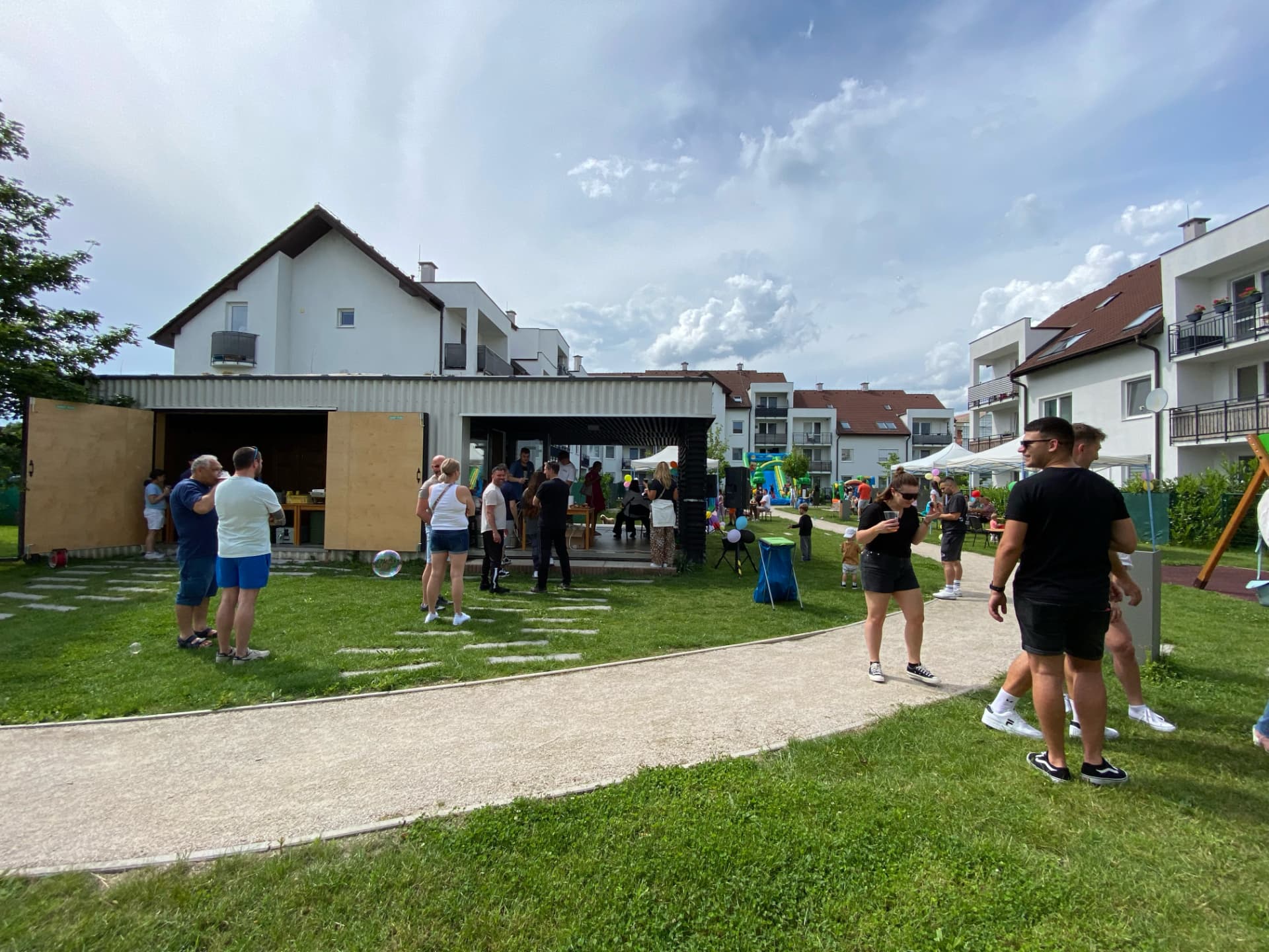 Letné susedské podujatie v projekte Polianky — rodiny na trávniku medzi bytovými domami, stánky a skákací hrad